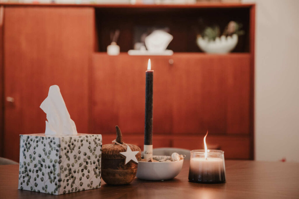 Stillvolle Trauerecke: Taschentücher, Holzbehälter mit Stern, schwarze Kerze, Schale und Glaslicht auf Tisch bei Lebenskreise Bestattungen.