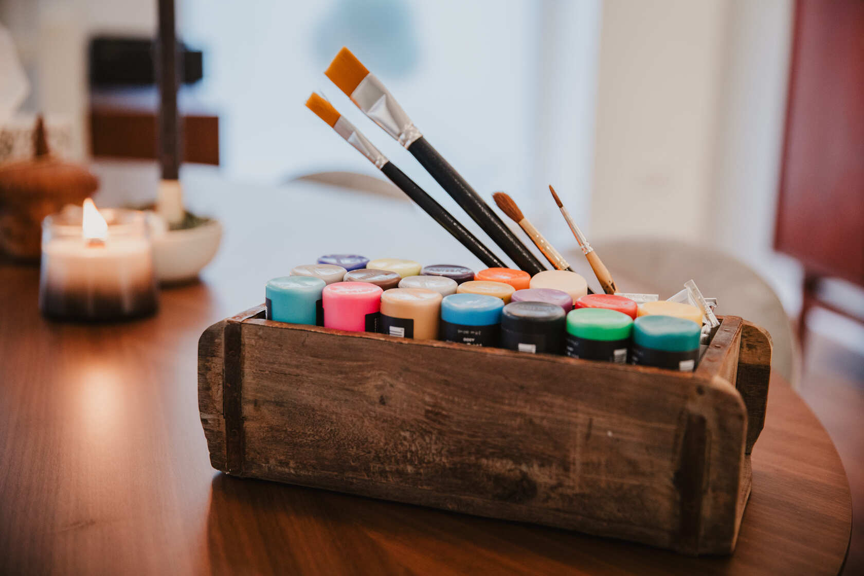 Auf einem Tisch steht eine Holzbox mit Farbtöpfen und Pinseln, daneben brennt eine Kerze - Bild aus unserer Trauerbegleitung.