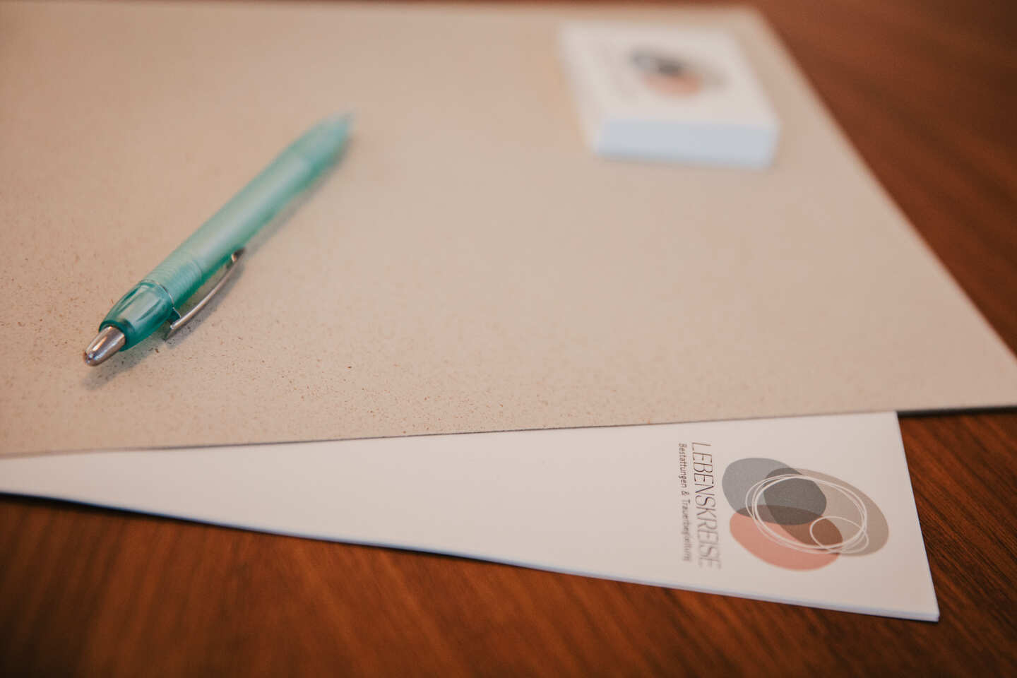 Broschüre von Lebenskreise Bestattungen, Stift und Radiergummi auf beige Mappe, Holztisch, Gau-Algesheim/Rheinhessen.