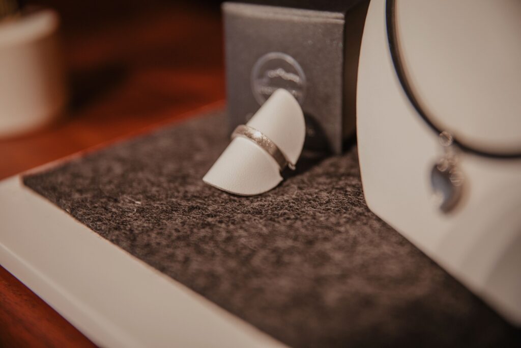 Ein silberner Ring auf weißem Ständer liegt auf grauem Filz, daneben eine Schmuckschachtel und eine schwarze Kette.